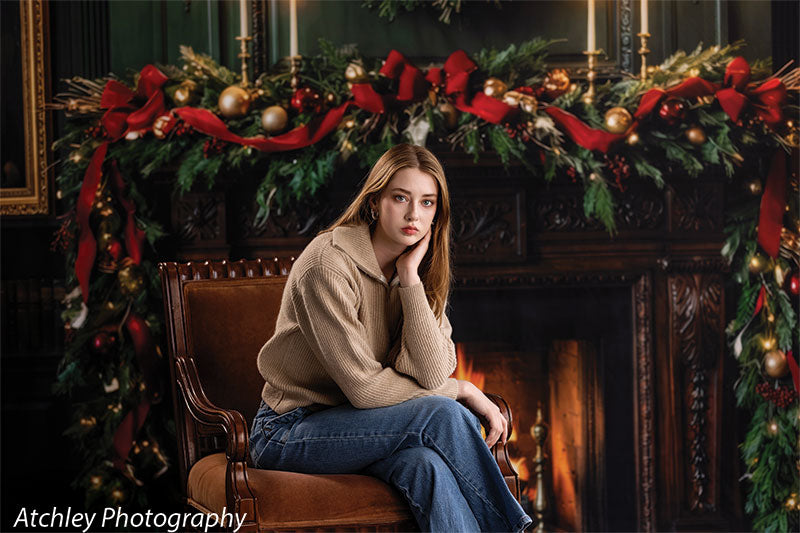 Manor Hearth dark wood fireplace with Christmas wreath photography backdrop shown with a senior girl seated by the fireplace in a thoughtful pose, wide view CP-8885