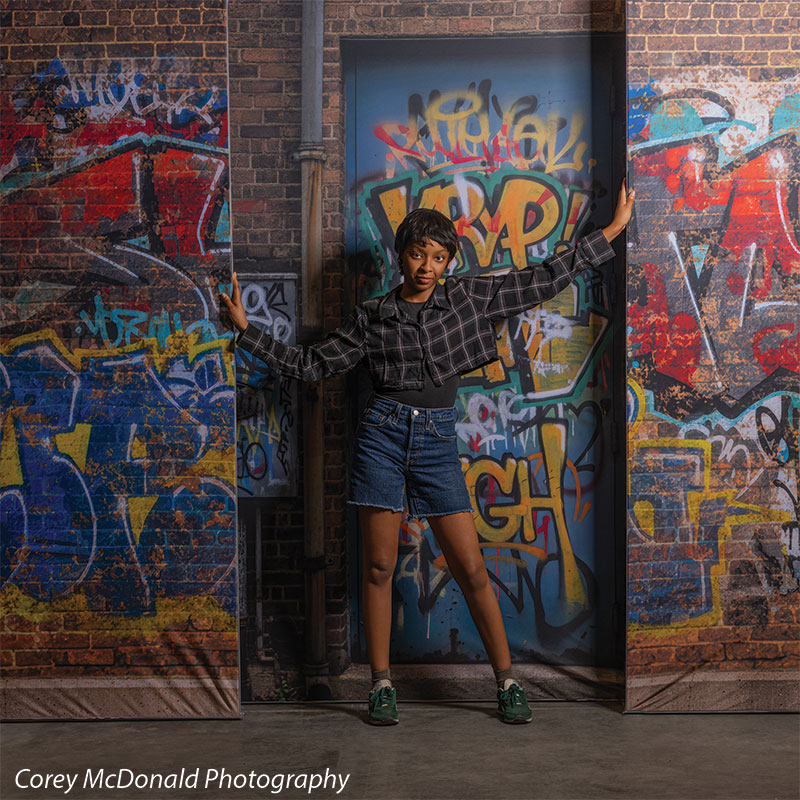 Marlowe Brick Wall Graffiti, photography backdrop panel for Denny StudioEdge silicone edge frame, shown with a senior girl standing with both arms spread against the graffiti wall SECP-8863