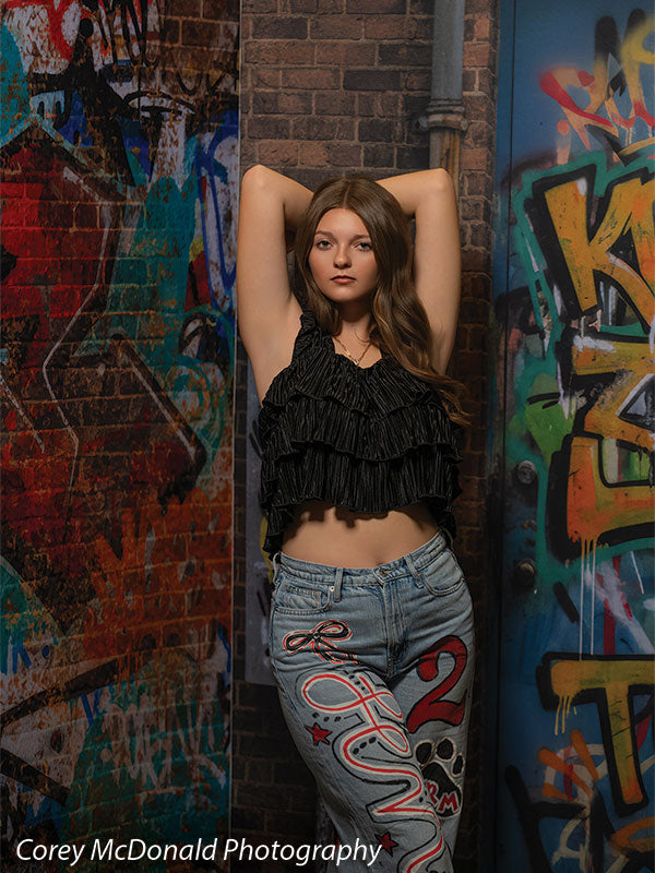Marlowe Brick Wall Graffiti, photography backdrop panel for Denny StudioEdge silicone edge frame, shown with a senior girl in a black ruffle top with both arms raised overhead SECP-8863