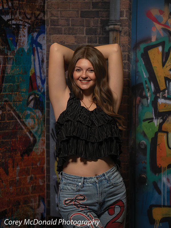 Marlowe Brick Wall Graffiti, photography backdrop panel for Denny StudioEdge silicone edge frame, shown with a senior girl in a black ruffle top smiling with arms overhead SECP-8863