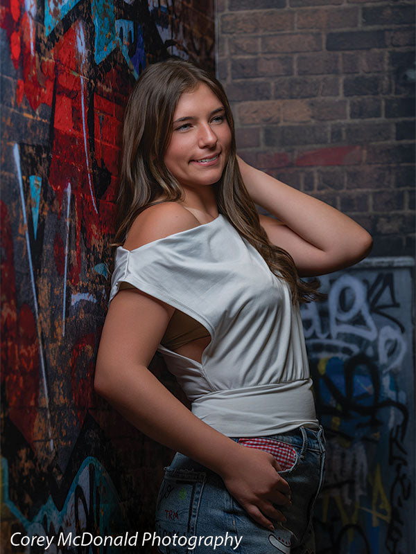 Marlowe Brick Wall Graffiti, photography backdrop panel for Denny StudioEdge silicone edge frame, shown with a senior girl in an off-shoulder white top smiling with a hand behind her neck SECP-8863