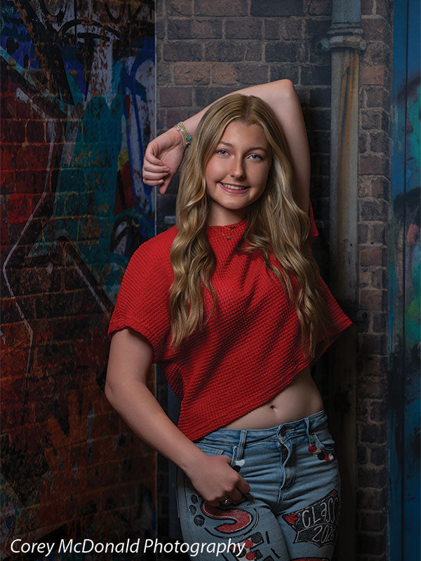 Marlowe Brick Wall Graffiti, photography backdrop panel for Denny StudioEdge silicone edge frame, shown with a senior girl in a red top with an arm resting up on the graffiti wall SECP-8863