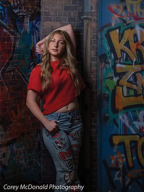 Marlowe Brick Wall Graffiti, photography backdrop panel for Denny StudioEdge silicone edge frame, shown with a senior girl in a red top and painted jeans leaning with an arm on the wall SECP-8863