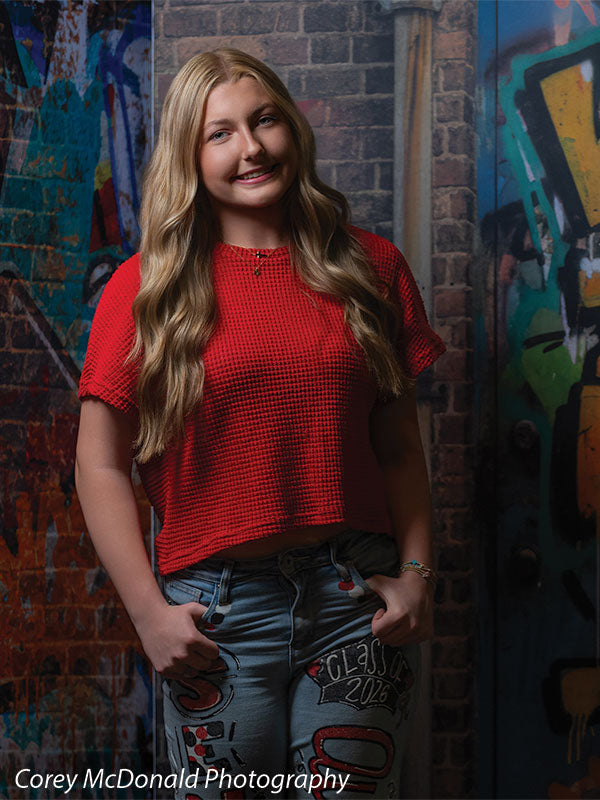 Marlowe Brick Wall Graffiti, photography backdrop panel for Denny StudioEdge silicone edge frame, shown with a senior girl in a red top and painted jeans smiling with hands in her pockets SECP-8863
