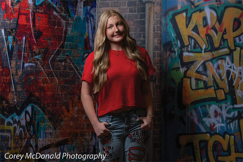 Marlowe Brick Wall Graffiti, photography backdrop panel for Denny StudioEdge silicone edge frame, shown with a senior girl in a red top standing in front of the graffiti wall SECP-8863