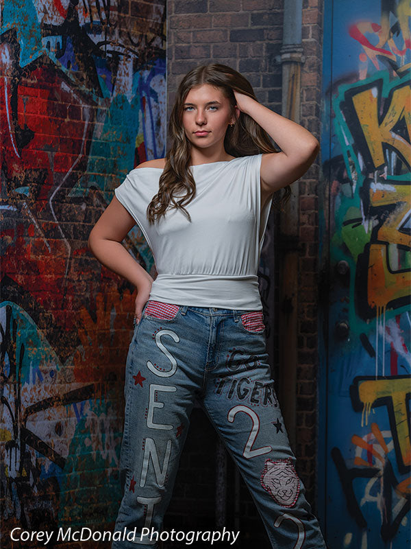 Marlowe Brick Wall Graffiti, photography backdrop panel for Denny StudioEdge silicone edge frame, shown with a senior girl in a white top and painted jeans with a hand in her hair SECP-8863