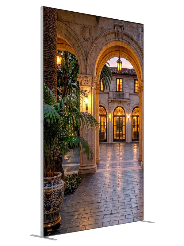 Grand stone archways opening onto a lantern-lit Mediterranean villa courtyard at dusk, 5ft photography backdrop panel for Denny StudioEdge silicone edge frame, angled view