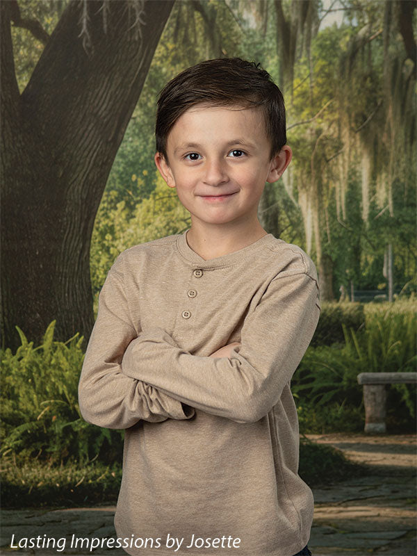 Moss Oak photography backdrop showing a grand Southern live oak draped in Spanish moss over a stone garden path, shown with a young boy in a tan henley with his arms crossed CP-8783