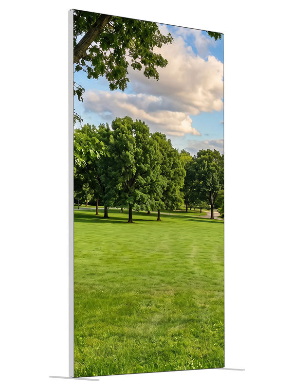 A broad open park lawn with a large shade tree and a distant tree line under a cloud-dotted sky, 4ft photography backdrop panel for Denny StudioEdge silicone edge frame, angled view