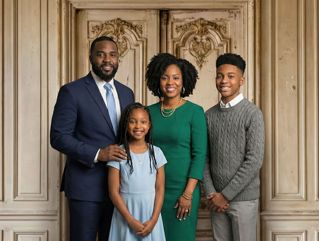 Family of four posing together with a father in a navy suit, mother in a green dress, daughter in a light blue dress, and teenage son in a gray sweater standing in front of an ornate vintage cream-colored double door backdrop with carved details.
