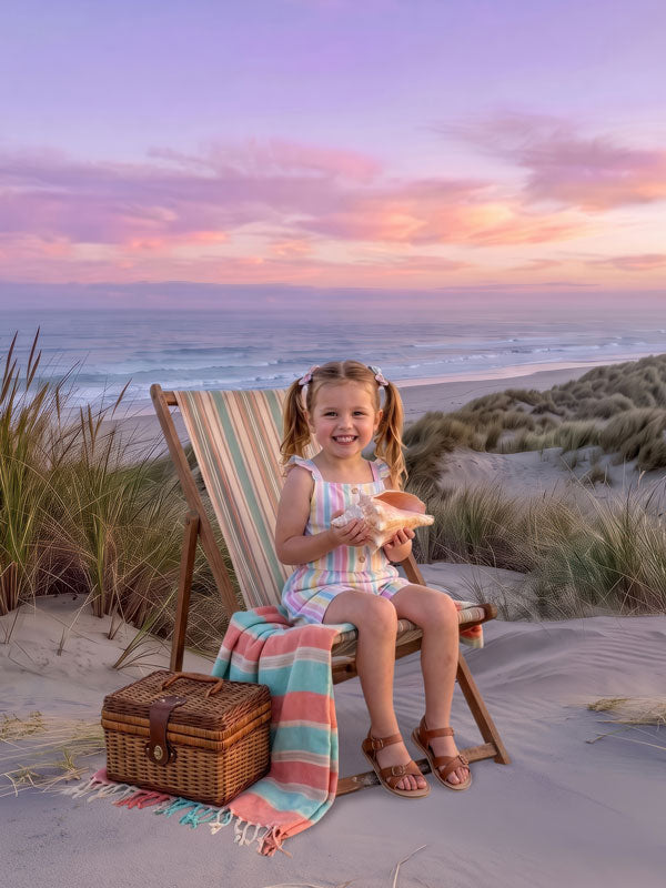 Pastel sunset beach dune photography backdrop shown in a summer studio portrait with a young girl in a striped romper seated in a beach chair holding a shell CP-9042