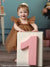 Baby girl in brown dress celebrating her first birthday in front of Peach Balloon Bliss Cake Smash Backdrop with large pink number one block.