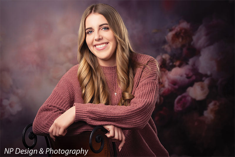 Peonies and roses photography backdrop shown with a senior girl in a mauve sweater leaning on the back of a wood chair, smiling CP-8491