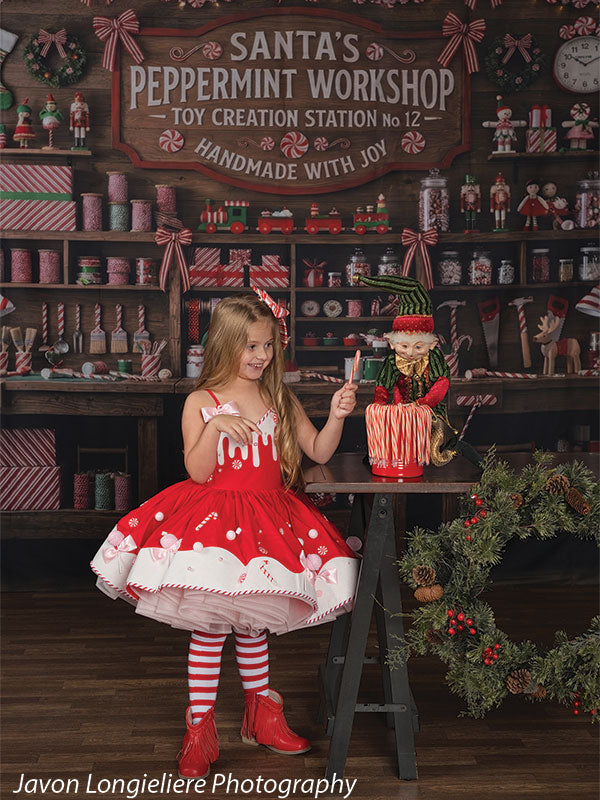 Peppermint Hollow Santa's peppermint workshop photography backdrop shown with a young girl in a red-and-white candy dress pointing a candy cane beside an elf figure CP-8912