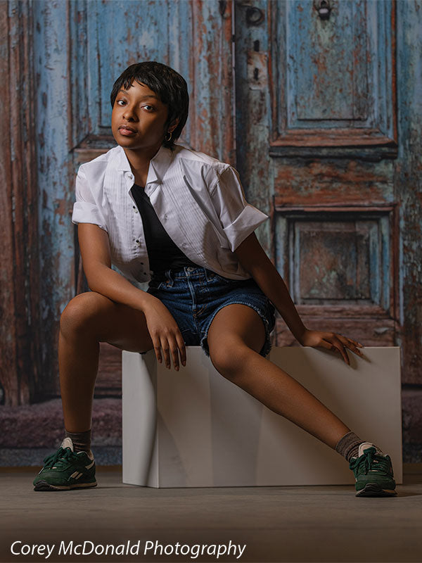 Photography posing cube shown with a senior girl seated on the white posing cube in a vertical portrait against a distressed blue-door backdrop PC