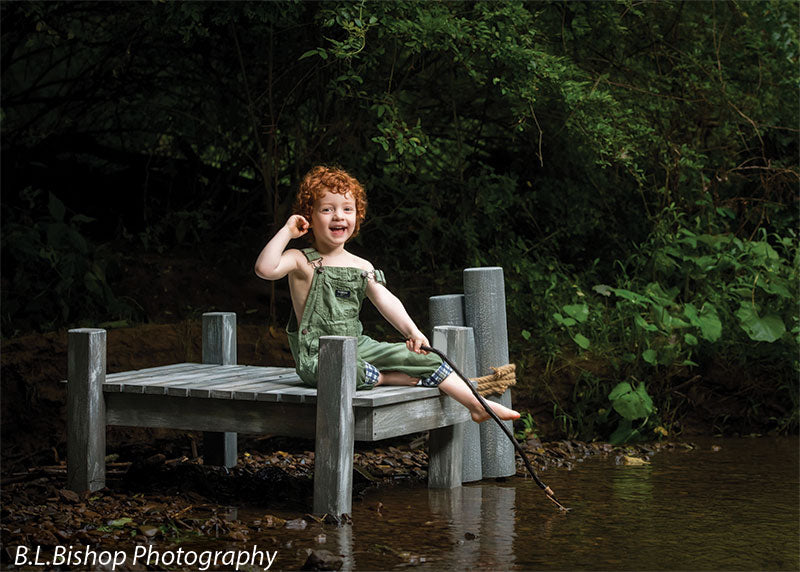 Pier and piling beach prop set shown with a red-haired toddler in green overalls smiling with one leg kicked out over the creek while holding the fishing line BEACH-SET