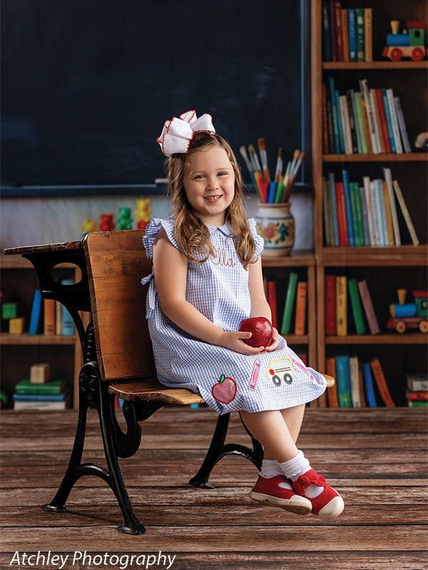 Reclaimed wood photography floor drop shown with a young girl in a blue gingham dress seated at an antique school desk on the reclaimed wood plank floor in a classroom scene FD-4070