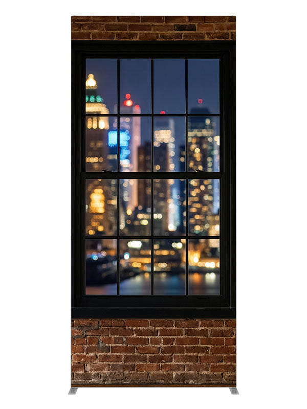 A red-brick industrial loft with black-framed windows over a nighttime city skyline in bokeh, 3ft photography backdrop panel for Denny StudioEdge silicone edge frame