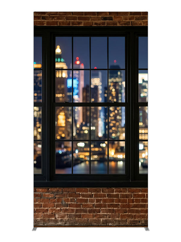 A red-brick industrial loft with black-framed windows over a nighttime city skyline in bokeh, 4ft photography backdrop panel for Denny StudioEdge silicone edge frame