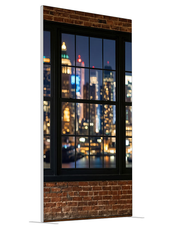 A red-brick industrial loft with black-framed windows over a nighttime city skyline in bokeh, 4ft photography backdrop panel for Denny StudioEdge silicone edge frame