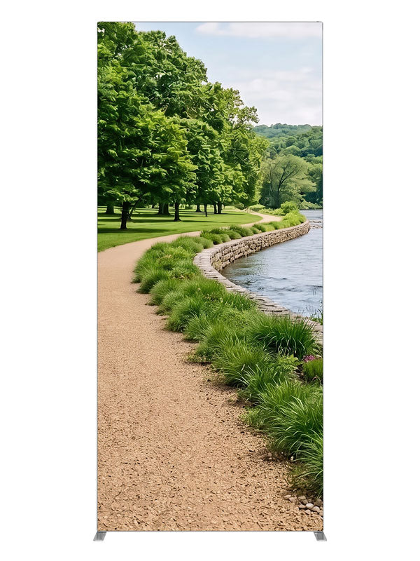 A gravel path along a calm river with a stacked-stone bank, grasses and a wooded far shore, 3ft photography backdrop panel for Denny StudioEdge silicone edge frame