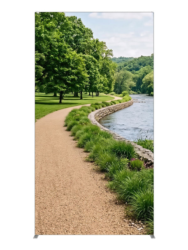 A gravel path along a calm river with a stacked-stone bank, grasses and a wooded far shore, 4ft photography backdrop panel for Denny StudioEdge silicone edge frame