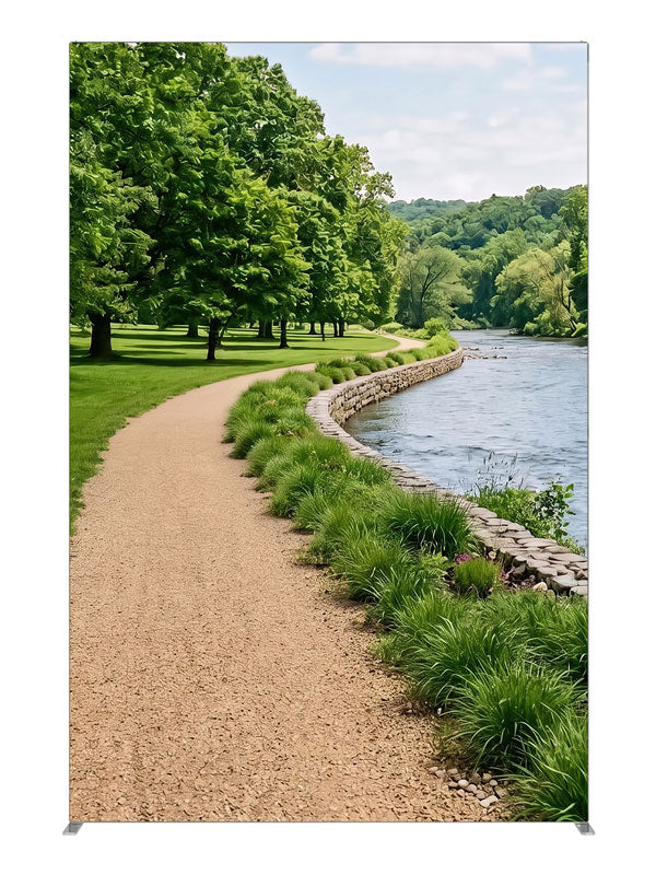 A gravel path along a calm river with a stacked-stone bank, grasses and a wooded far shore, 5ft photography backdrop panel for Denny StudioEdge silicone edge frame