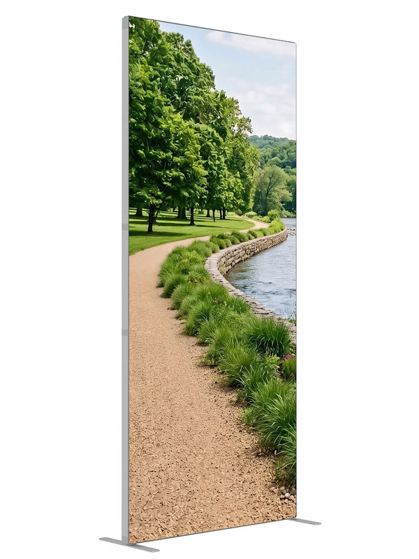 A gravel path along a calm river with a stacked-stone bank, grasses and a wooded far shore, 3ft photography backdrop panel for Denny StudioEdge silicone edge frame, angled view
