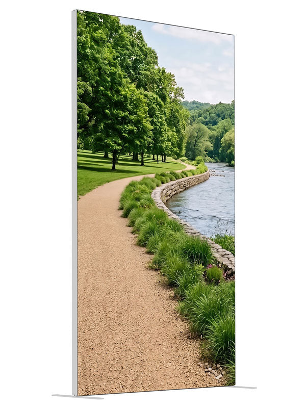A gravel path along a calm river with a stacked-stone bank, grasses and a wooded far shore, 4ft photography backdrop panel for Denny StudioEdge silicone edge frame, angled view