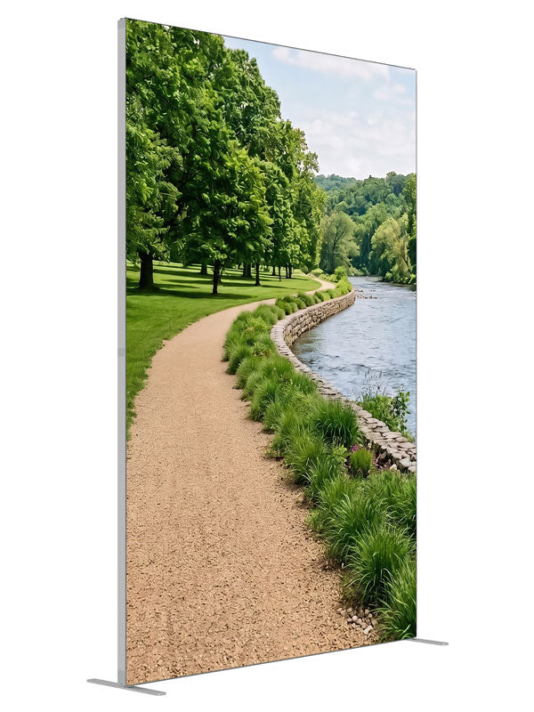 A gravel path along a calm river with a stacked-stone bank, grasses and a wooded far shore, 5ft photography backdrop panel for Denny StudioEdge silicone edge frame, angled view