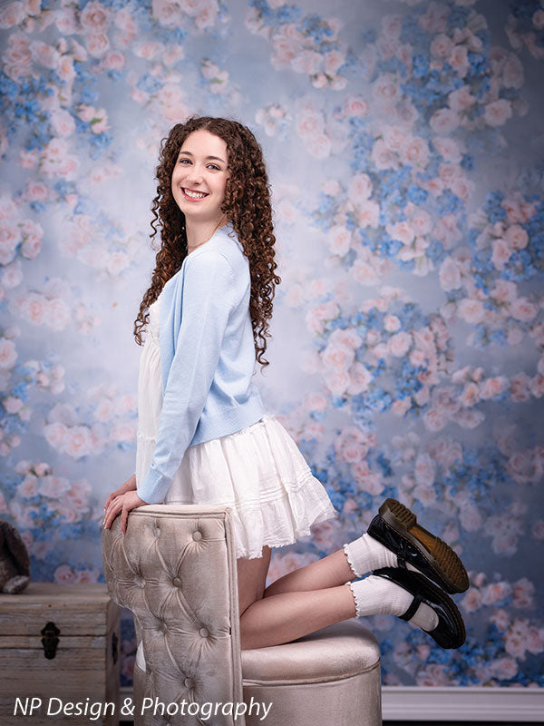 Rose master blue floral photography backdrop shown with leaning on a round ottoman in a full-length pose turning toward the camera CP-7598