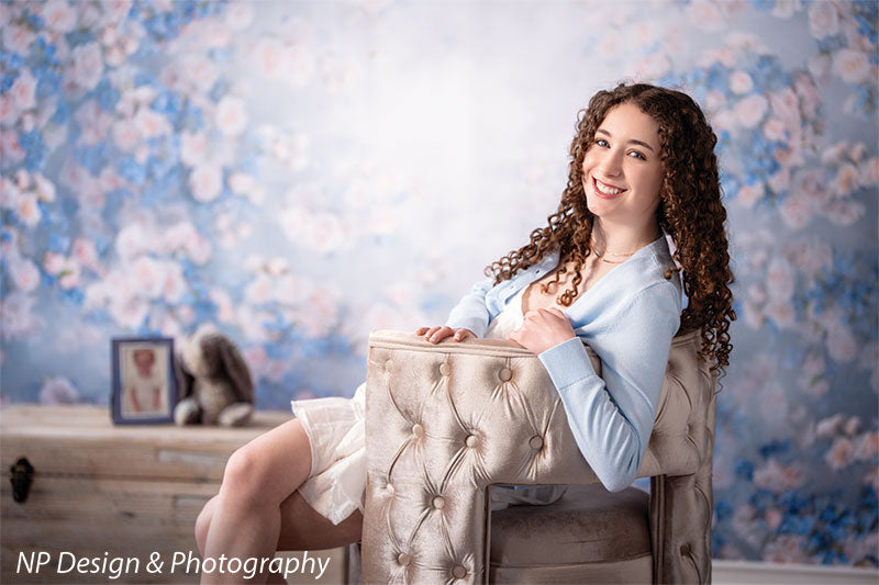 Rose master blue floral photography backdrop shown with seated in a cream tufted armchair holding a pillow and smiling CP-7598