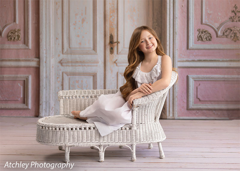 Rose Parlor distressed pink French double doors photography backdrop shown with a young girl seated on a white wicker settee in a wide view CP-8793