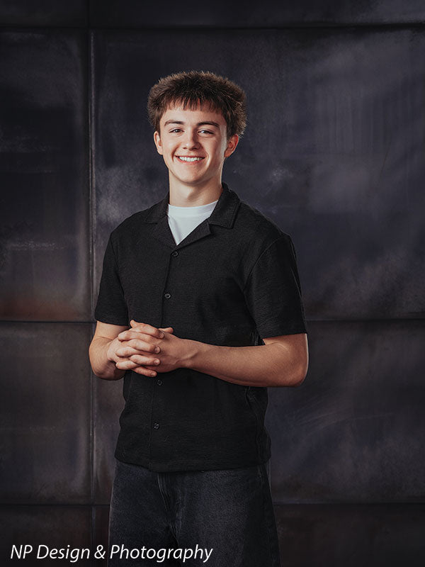 Rustic industrial metal panels photography backdrop shown with a senior boy in a black shirt with his hands clasped in front, smiling CP-8431