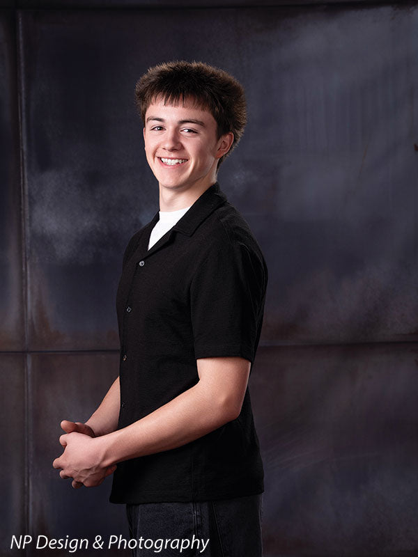 Rustic industrial metal panels photography backdrop shown with a senior boy turned three-quarters with his hands clasped, smiling CP-8431