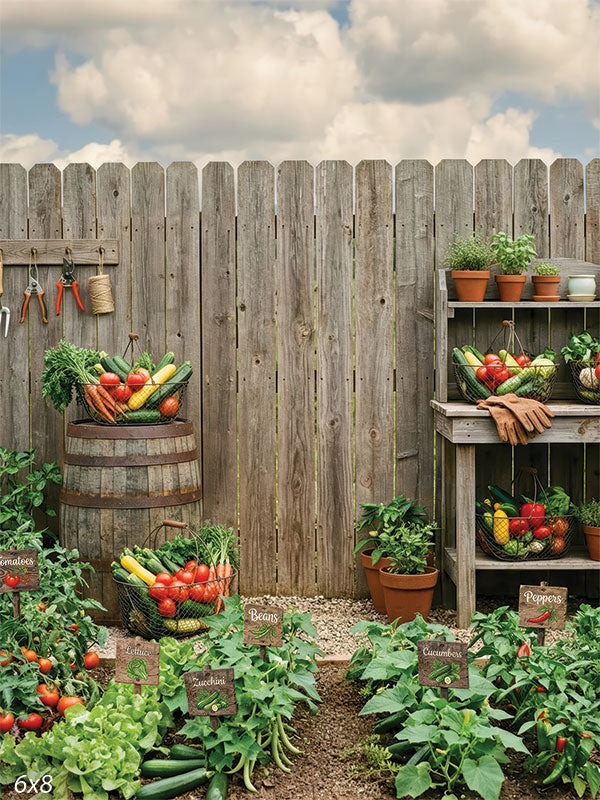 Printed photography backdrop showing a rustic vegetable garden with a weathered wooden fence, wooden barrel, and garden tools.
