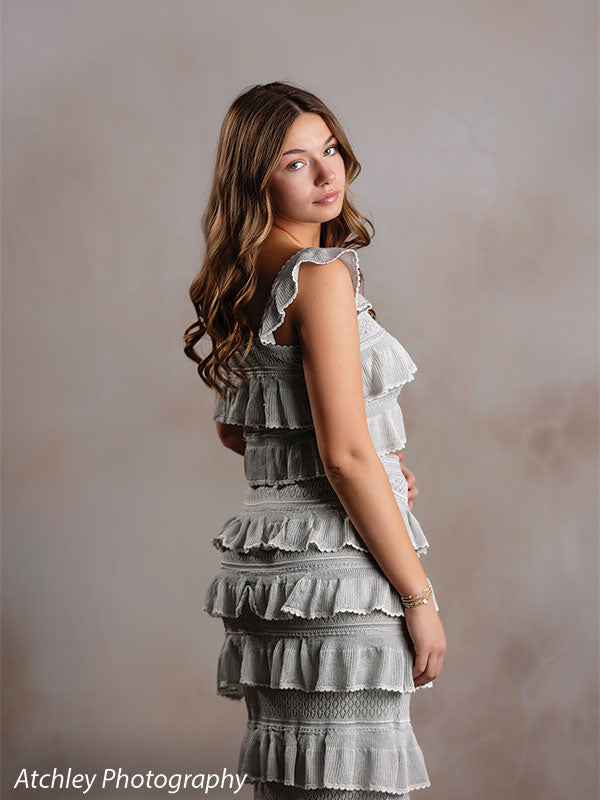 Sand Plaster warm cream plaster texture photography backdrop shown with a senior girl in a sage-green ruffled dress glancing over her shoulder CP-8762
