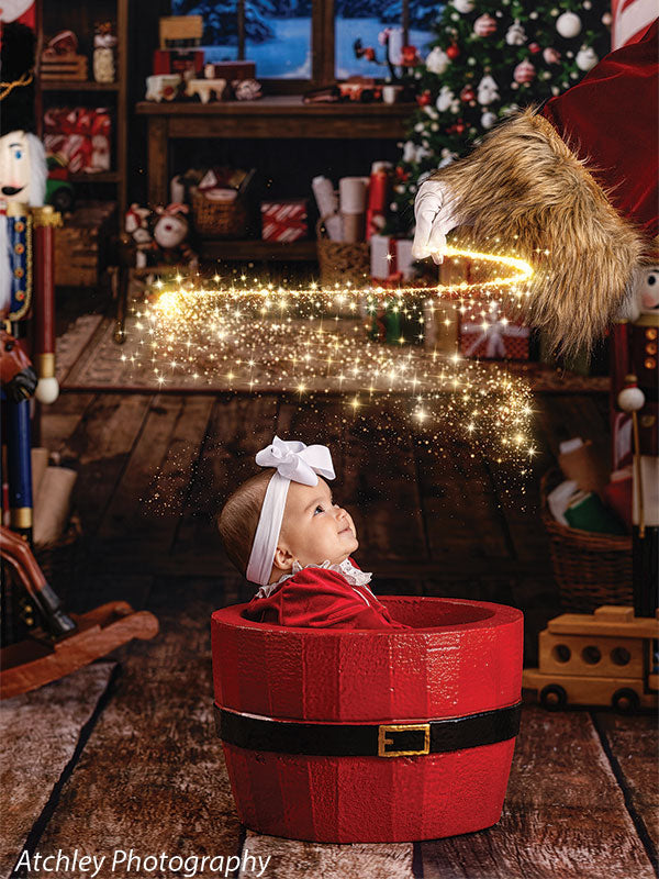 Santa Basket photography prop shown with a baby in the red Santa basket looking upward in a Christmas workshop scene SNTA-BSKT
