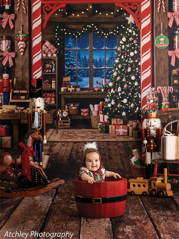Santa Basket photography prop shown with a baby seated inside the red Santa-belt basket in a Christmas workshop scene SNTA-BSKT