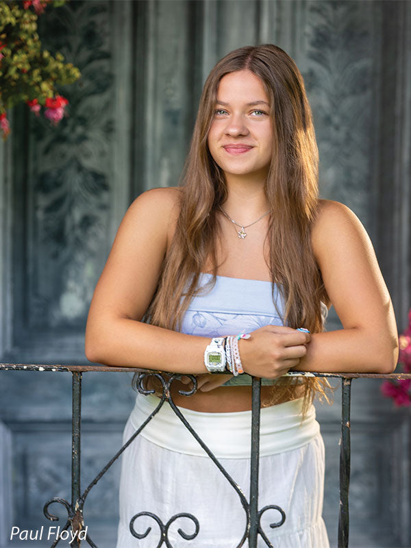 Slate Chateau photography backdrop showing distressed blue-grey carved double doors with pink blossoms, shown with a senior girl in a white top and long white skirt standing at an iron rail CP-8792