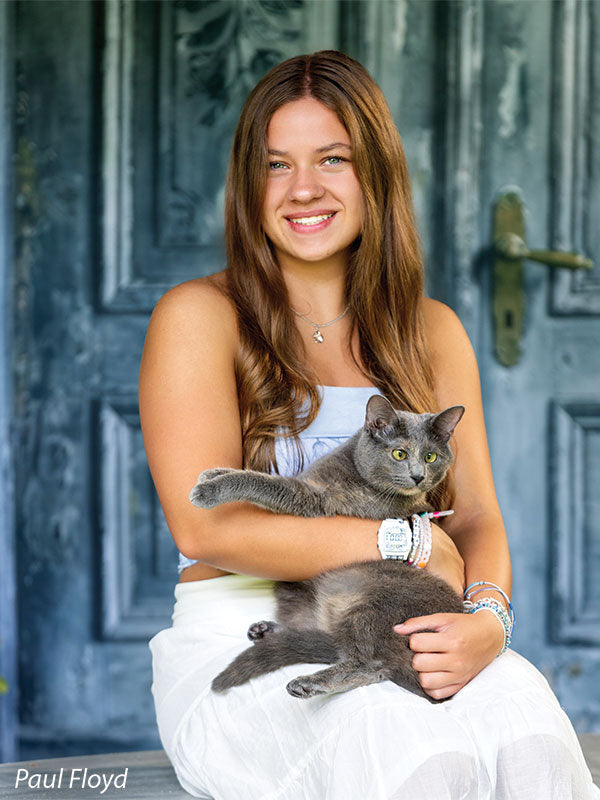Slate Chateau photography backdrop showing distressed blue-grey carved double doors with pink blossoms, shown with a senior girl in a white outfit seated holding a gray cat on her lap CP-8792