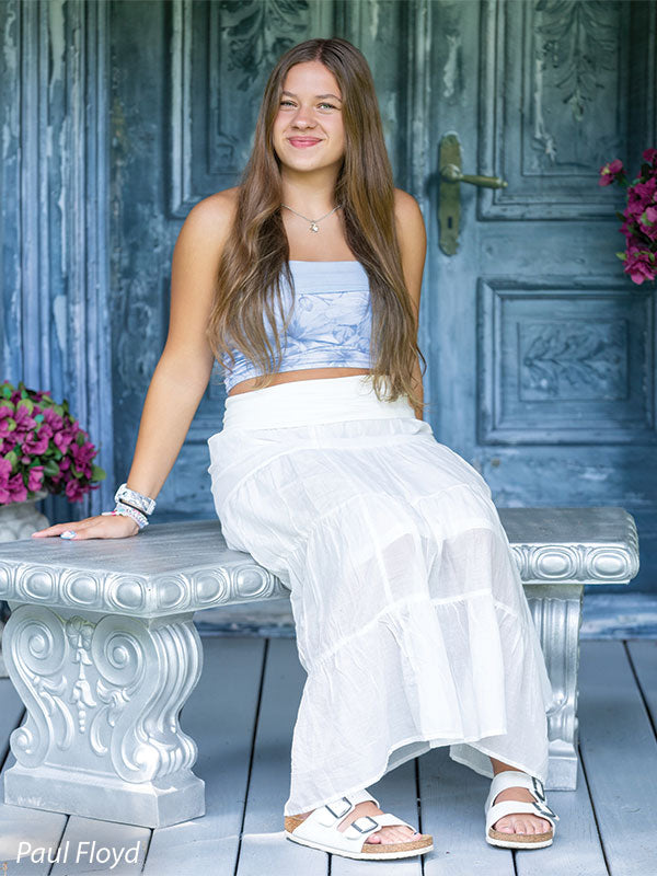 Slate Chateau photography backdrop showing distressed blue-grey carved double doors with pink blossoms, shown with a senior girl in a white outfit seated on an ornate stone bench CP-8792