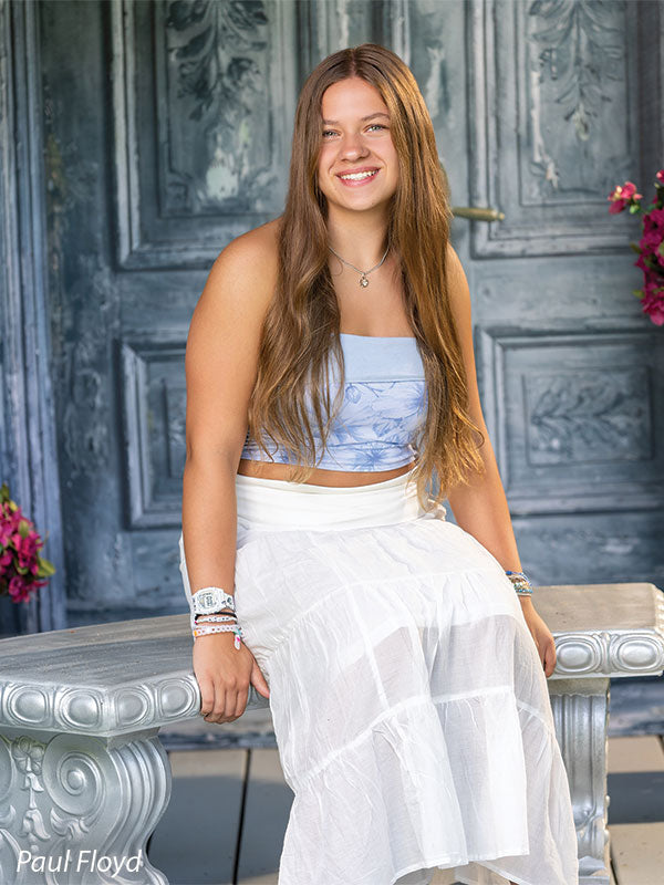 Slate Chateau photography backdrop showing distressed blue-grey carved double doors with pink blossoms, shown with a senior girl in a white outfit seated on the stone bench in a side profile CP-8792