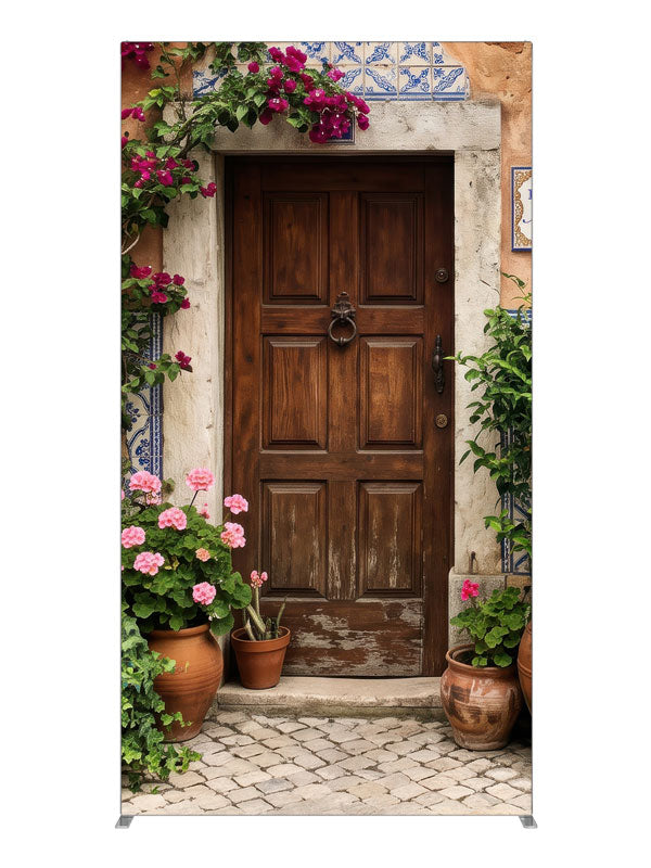 A carved wood door in a peach-terracotta Spanish facade with bougainvillea and potted geraniums, 4ft photography backdrop panel for Denny StudioEdge silicone edge frame