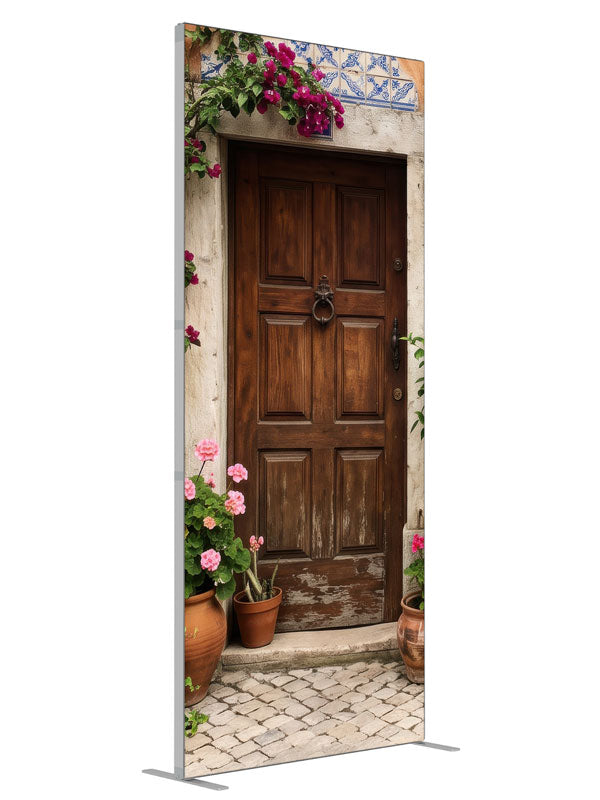 A carved wood door in a peach-terracotta Spanish facade with bougainvillea and potted geraniums, 3ft photography backdrop panel for Denny StudioEdge silicone edge frame, angled view