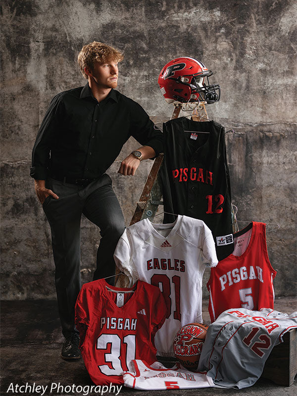Grunge gray sports photography backdrop featuring multiple Pisgah and Eagles jerseys, helmet, and props, with a senior boy posed for a dynamic athlete portrait.