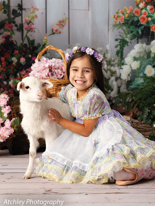 Pastel flower photography backdrop with a girl in a spring dress and floral crown posing with a lamb, perfect for Easter and spring portraits.