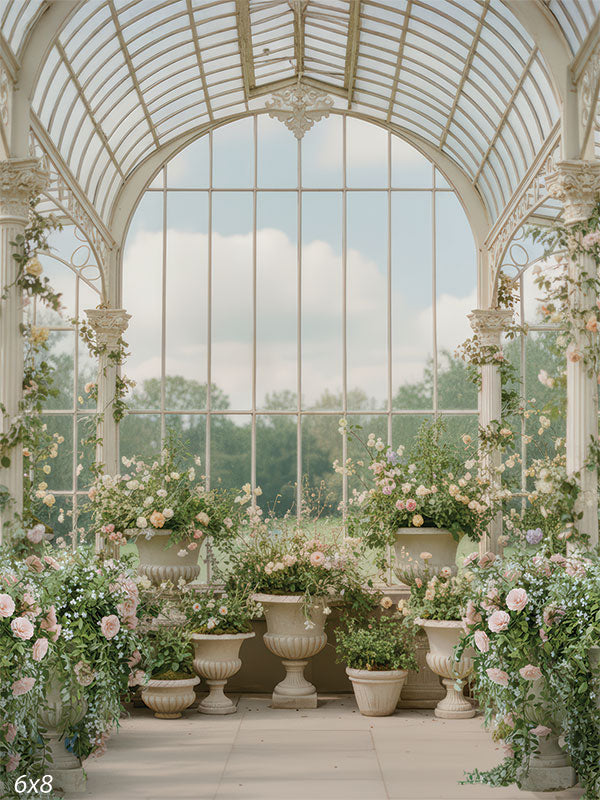 A bright spring conservatory scene with arched glass windows, ivory framework, and soft blush and cream florals arranged in classical urns.