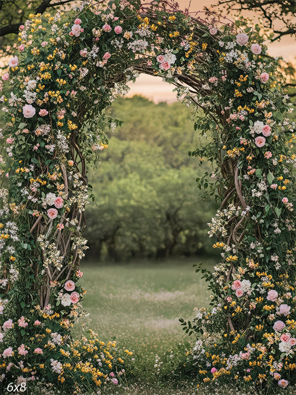 Lush woodland floral arch backdrop, with twisting branches covered in pink roses, yellow flowers, and greenery opening onto a soft meadow.