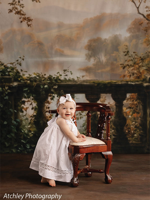 Stained concrete photography floor drop shown with a baby girl in a white dress standing at an antique chair on the stained concrete floor before a misty autumn valley backdrop FD-4148